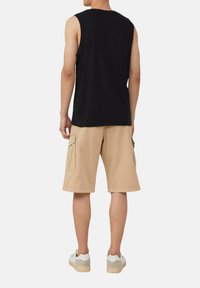 Schwarzes ärmelloses Shirt, beiges Cargo-Shorts mit Seitentaschen, weiße Sneaker mit grauen Akzenten, aufrecht stehend, von hinten gesehen.