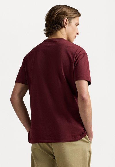 Burgundy kortärmad t-shirt med avslappnad passform, tillverkad av bomull, med rund halsringning och slät textur. Bakifrån syns minimala detaljer.
