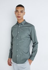 Camisa de botones de color verde oscuro con un cuello clásico, mangas largas y una textura suave, adornada con botones blancos en el frente.
