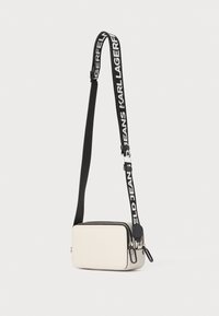 Rectangular crossbody bag in smooth cream leather with a zipper closure. Features a black woven strap with white branding accents.