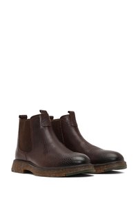 Botas Chelsea de cuero marrón con superficie texturizada, paneles elásticos laterales y una suela de goma contrastante. Diseño clásico con detalles mínimos.