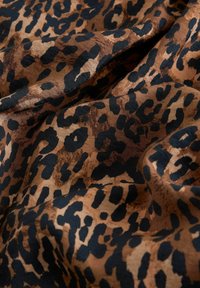 Tkanina s leopard uzorkom koja se sastoji od mešavine smešnih i crnih tonova, sa mekom teksturom i nepravilnim oblicima koji podsećaju na životinjske tačke.
