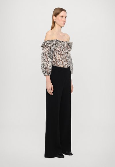 Bluză florală fără umeri din material transparent, completată cu un decolteu elastic cu volane. Asortată cu pantaloni evazați negri cu talie înaltă.