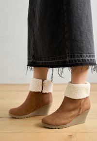 Botas de cano baixo castanhas com um punho em pelo falso, material de camurça suave, fecho lateral com zíper e sola de borracha texturizada.