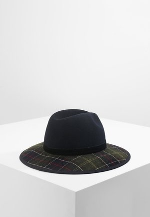 Chapeau fedora en feutre noir avec un large bord à carreaux vert foncé, rouge et blanc, présenté sur une surface blanche sur fond neutre.
