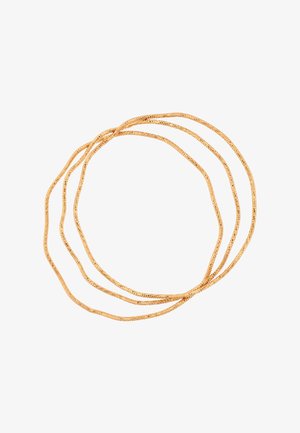 Drie dunne gouden kettingen losjes opgerold tegen een witte achtergrond, waarbij hun fijne, reflecterende textuur wordt benadrukt.