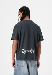 Tmavošedé tričko s krátkym rukávom vyrobené z bavlny, so veľkým bielym grafickým motívom "Cypress Hill" na zadnej strane, uvoľneného strihu a okrúhlym výstrihom.