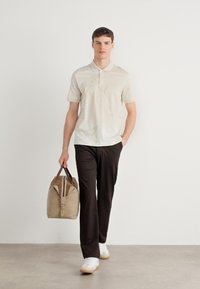 Šviesiai ruda polo marškinėliai, juodos kelnės, baltos sportinės bateliai; nešasi šviesiai rudos sportinės kuprinės su rudos spalvos diržais. Minimalistinis dizainas, lygus tekstūros.