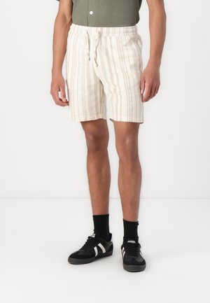 Shorts en mélange de lin crème avec des rayures verticales beiges, dotés d'une taille élastique et d'un cordon de serrage, accompagnés de baskets noires et de chaussettes.