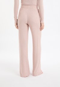 Pantaloni da lounge rosa chiaro a coste con orlo svasato e cintura elastica, che mostrano una texture morbida e dettagli di cucitura sottili.