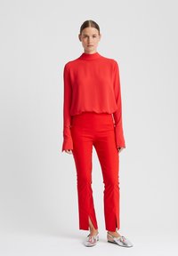 Rode top met lange mouwen en hoge hals, gecombineerd met rood, hooggetailleerd broek met zijopeningen. Zilveren instapschoenen zorgen voor een reflecterend detail.