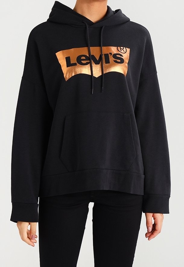 Personne portant un sweat à capuche noir avec une poche avant et un logo Levi's cuivre brillant sur la poitrine.