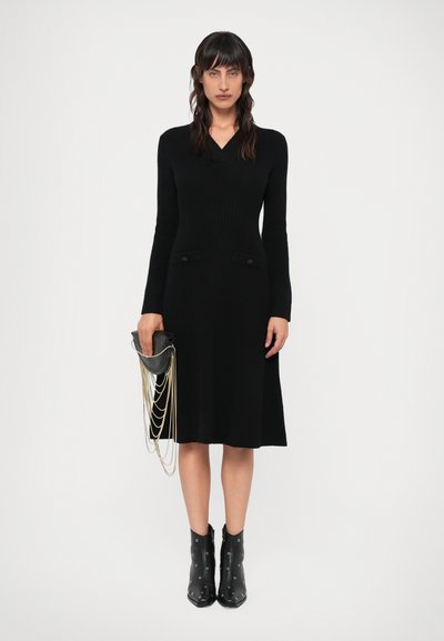 Vestido preto de mangas longas com decote em V, textura canelada e dois bolsos frontais. Combinado com uma bolsa preta de mão com correntes douradas e botas ankle.