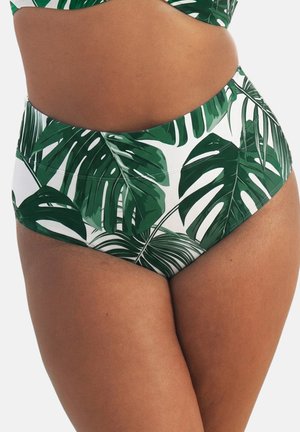 Person trägt hochgeschnittene Bikinihosen mit grünem tropischem Blättermuster auf weißem Hintergrund, zu sehen von der Taille bis zum mittleren Oberschenkel.
