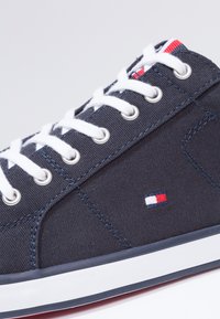 Sneaker in tela blu navale con lacci bianchi, occhielli argentati e logo rosso, bianco e blu. Presenta una suola in gomma e cuciture in contrasto.