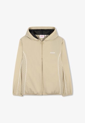 Veste légère beige avec capuche, fermeture éclair à l'avant et accents blancs. Comprend une doublure en mesh et des détails perforés sur les côtés.