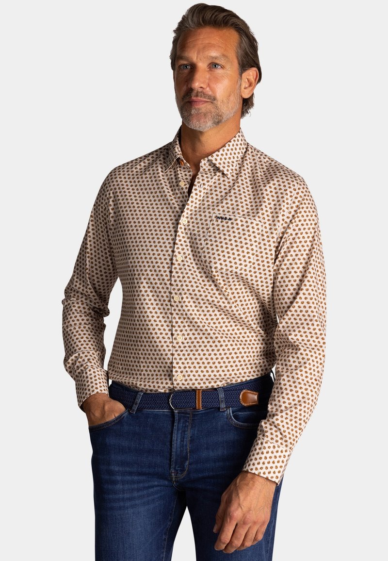 Heren overhemd met knoopsluiting in lichtbeige met een bruin stippenpatroon, lange mouwen en een borstzak. Draagt met donkerblauwe jeans en een blauwe riem.