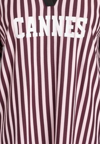 Camicia a righe maroon e rosa con scollo a V, con grande testo bianco "CANNES" sulla parte anteriore. Realizzata in un tessuto testurizzato.