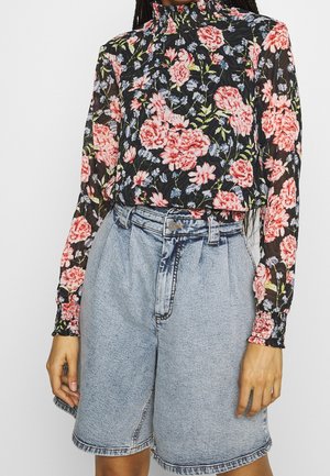 Haut à manches longues fleuri avec un col montant en noir, orné de fleurs roses et bleues. Associé à un short en denim bleu clair à coupe décontractée.