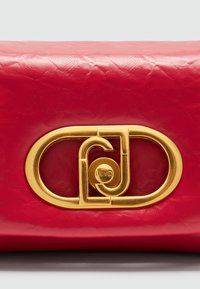 Rote Leder-Clutch mit strukturiertem Oberflächenmaterial, ausgestattet mit einem auffälligen goldenen, runden Schlossverschluss mit verflochtenen Initialen.