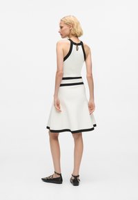 Fehér ujjatlan ruha fekete részletekkel, testhez simuló felső résszel, bővülő szoknyával és kulcslyuk hátkivágással. Texturált anyag, térd középig érő fazon.