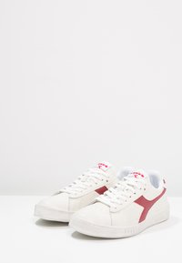 Scarpe sportive bianche con logo e dettagli rossi, tomaia in pelle texture, punta rotonda, design con lacci e suola in gomma.