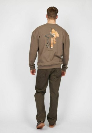 Brun sweatshirt med et løvegrafik på ryggen, parret med olivengrønne bukser. Tekstureret stof, rund halsudskæring og afslappet pasform.