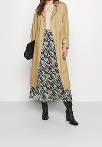 Beige trench coat dengan aksesoris perak, dipadukan dengan rok bermotif hitam-putih dan sepatu bot hitam setinggi lutut. Tas hitam sederhana.