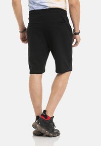 Zwarte katoenen shorts met een relaxte pasvorm, voorzien van zijzakken en een comfortabele elastische tailleband. Gemaakt in combinatie met zwart-rode sneakers.