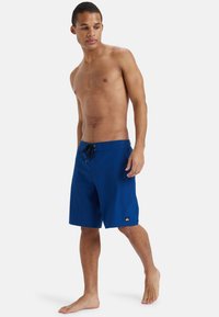 Blå badshorts i lättviktigt material. Har snörning i midjan och en liten logodetalj på vänster ben. Slät textur.