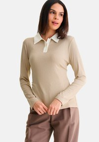 Beige langemouwen ribgebreide polo met een witte kraag en knopenlijst, gecombineerd met bruine broek met een zachte textuur.