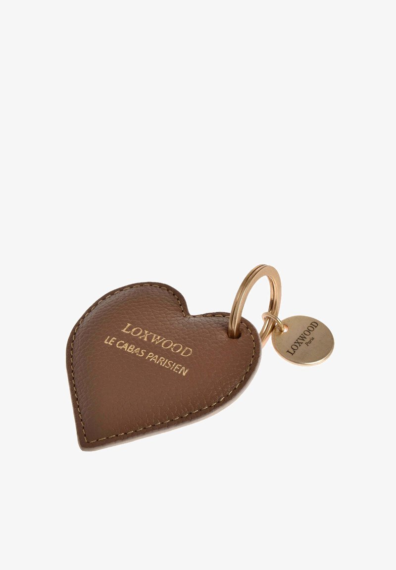 Porte-clés en cuir marron en forme de cœur avec des coutures dorées et un anneau doré, gravé avec "LOXWOOD LE CABAS PARISIEN" et une petite étiquette ronde.