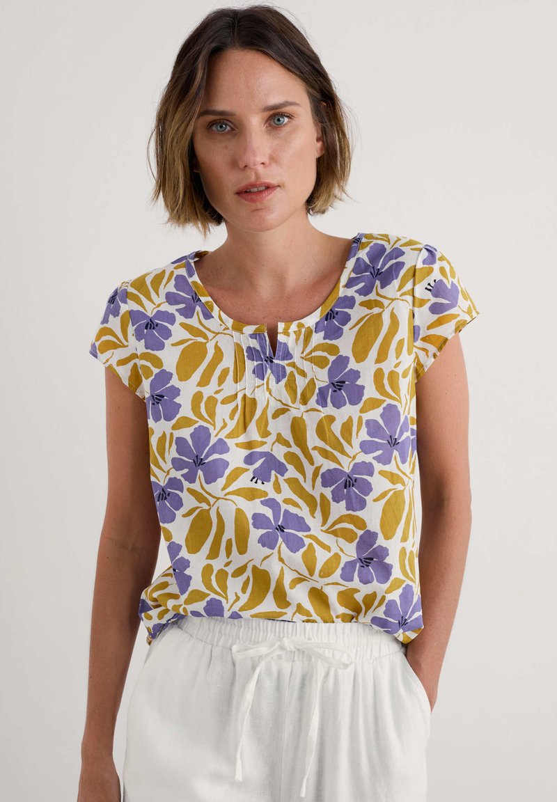 Bluză cu mânecă scurtă, florală, de culoare albă, cu modele în tonuri de mov și galben, având un guler rotund și un detaliu pliat scurt în față.