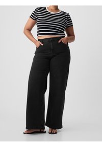 Jean noir à jambes larges, taille haute, poches avant, et un haut court à manches courtes rayé noir et blanc avec un col rond.