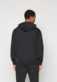 Črna kapuca s sproščenim prileganjem, rebrastimi manšetami in robom. Mehka, teksturirana tkanina. Na sprednji strani je kenguru žep.