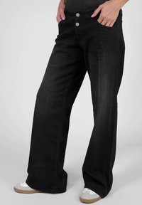 Jean en denim noir délavé avec des jambes évasées, deux poches avant et des boutons en métal argenté. Texture lisse, design décontracté.