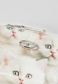 Portefeuille blanc avec une finition brillante et un motif de chatons blancs expressifs. Quincaillerie en argent avec un accent de logo stylisé.