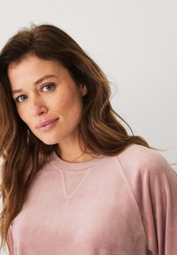 Lichtroze sweatshirt met een ronde hals en raglanmouwen, gemaakt van zachte stof. Een subtiele glans en textuur zijn zichtbaar op het oppervlak.