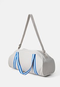 Saco de duffel cinza com alças listradas em azul e branco, tecido macio, forma cilíndrica, abertura superior com fecho éclair e uma alça de ombro destacável.