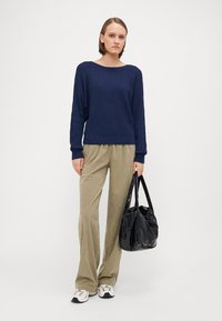 Marineblauw ribbeltrui, beige corduroy wijde broek en een zwarte glanzende tas. Sneakers met een metalen accent maken de outfit compleet.