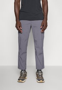 Gray, lightweight, stretch fabric pants with a smooth texture and side seams. Paired with black and tan athletic shoes featuring laces.