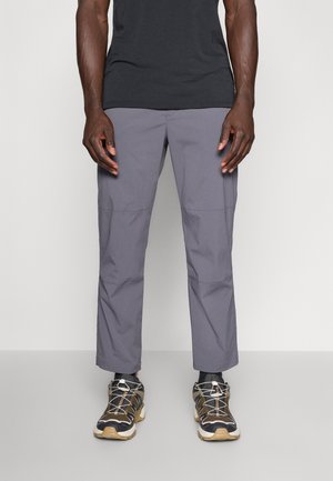 Pantaloni grigi, leggeri, in tessuto elasticizzato con una texture liscia e cuciture laterali. Abbinati a scarpe da ginnastica nere e tortora con lacci.