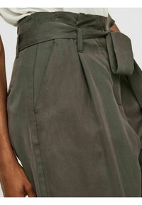 Oliivinvihreät korkeat housut, joissa on leveä vyö, laskostettu muotoilu, kaksi sivutaskua ja tekstuuriaines.