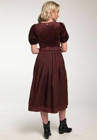 Bordeauxfarbenes Kleid mit Puffärmeln, tailliertem Oberteil und plissiertem Rock. Strukturierter Stoff mit feinem geometrischen Muster. Schwarze Knöchelboots.