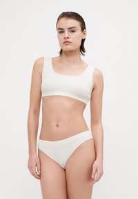 Kreminė medvilninė braletė su kvadratine iškirpte, derinama su atitikties žemai stovinčiomis bikini kelnaitėmis; glotni tekstūra, minimalistiškas dizainas ir be siūlių kraštai.