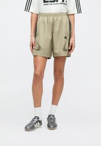 Khaki sport rövidnadrág elasztikus derékpánttal, oldalzsebekkel és sötét részletekkel. Szürke focicipővel és fehér zoknival párosítva.