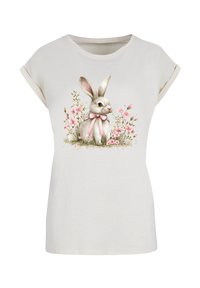 Light beige t-shirt with rolled sleeves, featuring an illustration of a rabbit with a pink bow, surrounded by pink flowers.