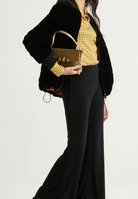 Veste bomber matelassée noire, blouse jaune à pois, pantalon noir à jambes larges, et sac à main doré orné de perles.