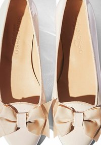 Bailarinas de charol en rosa pálido con un lazo texturizado en color beige. Interior suave con logo de la marca grabado. Diseño de punta redondeada.