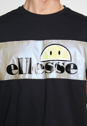 Schwarzes Hemd mit einem breiten silbernen horizontalen Streifen, der das "ellesse"-Logo in Schwarz und ein halbkreisförmiges Tennisball-Design über dem Text zeigt.